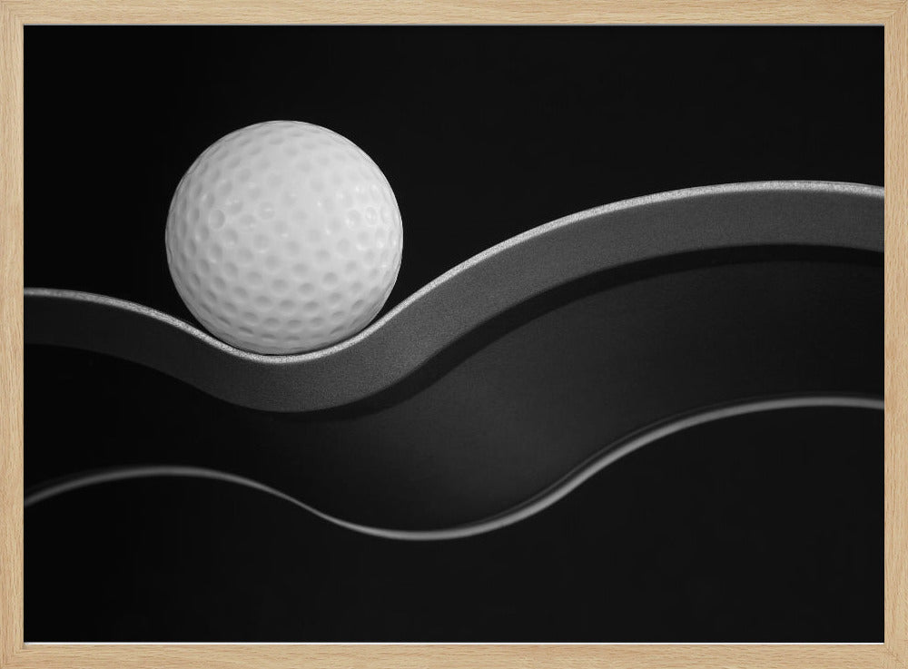 A framed, minimalist black and white photograph of a golf ball resting on a gracefully curving gray surface against a solid black background. Wall Art