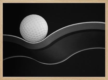 A framed, minimalist black and white photograph of a golf ball resting on a gracefully curving gray surface against a solid black background. Wall Art