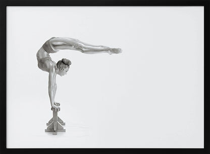 A framed black and white photograph of a female gymnast with a metallic silver-painted body, balancing in a difficult handstand pose on small blocks against a stark white background. Her back is arched and her legs are extended straight out behind her, parallel to the ground. Artwork