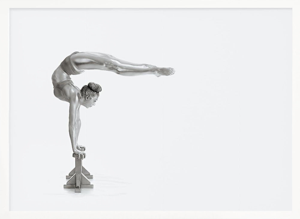 A framed black and white photograph of a female gymnast with a metallic silver-painted body, balancing in a difficult handstand pose on small blocks against a stark white background. Her back is arched and her legs are extended straight out behind her, parallel to the ground. Artwork