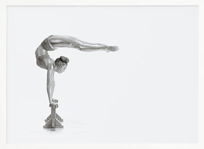 A framed black and white photograph of a female gymnast with a metallic silver-painted body, balancing in a difficult handstand pose on small blocks against a stark white background. Her back is arched and her legs are extended straight out behind her, parallel to the ground. Artwork