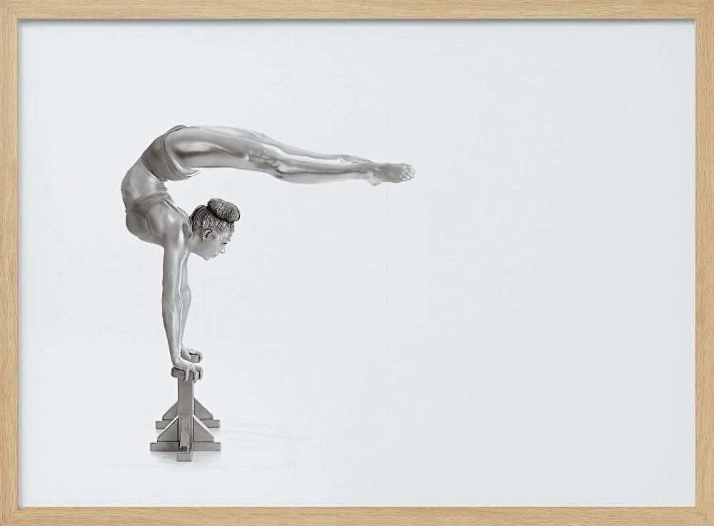 A framed black and white photograph of a female gymnast with a metallic silver-painted body, balancing in a difficult handstand pose on small blocks against a stark white background. Her back is arched and her legs are extended straight out behind her, parallel to the ground. Artwork