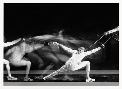 A framed, dramatic black and white photograph using long exposure to capture a fencer in motion. The fencer, in full white gear, lunges forward, their form crisp at the end of the movement while a ghostly blur trails behind, illustrating their rapid advance against a black background. Decor