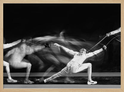 A framed, dramatic black and white photograph using long exposure to capture a fencer in motion. The fencer, in full white gear, lunges forward, their form crisp at the end of the movement while a ghostly blur trails behind, illustrating their rapid advance against a black background. Decor