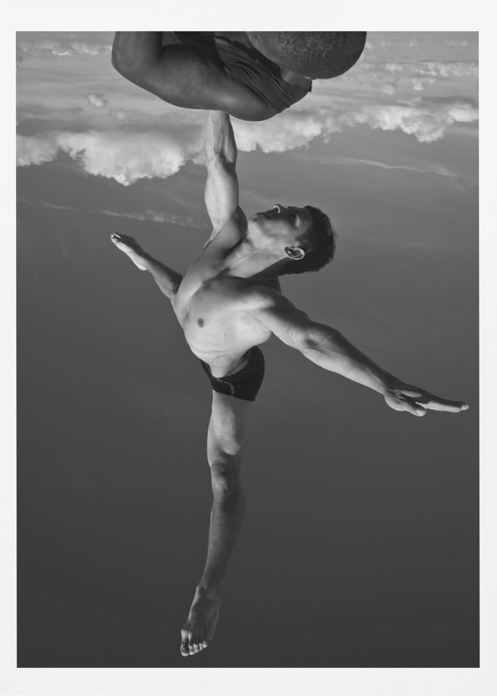 A surreal black and white photograph of two male acrobats. One man, in a graceful dance-like pose balancing on one leg, holds another man aloft with a single outstretched arm. The man being held is upside down against a backdrop of clouds, creating a gravity-defying and artistic illusion. Print