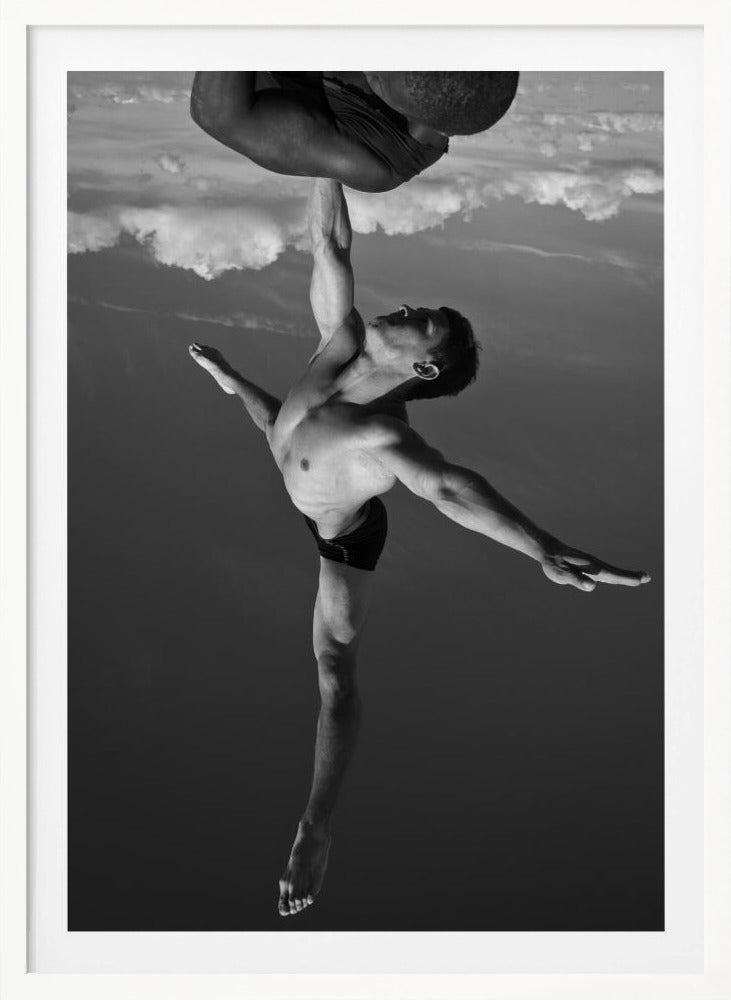 A surreal black and white photograph of two male acrobats. One man, in a graceful dance-like pose balancing on one leg, holds another man aloft with a single outstretched arm. The man being held is upside down against a backdrop of clouds, creating a gravity-defying and artistic illusion. Print