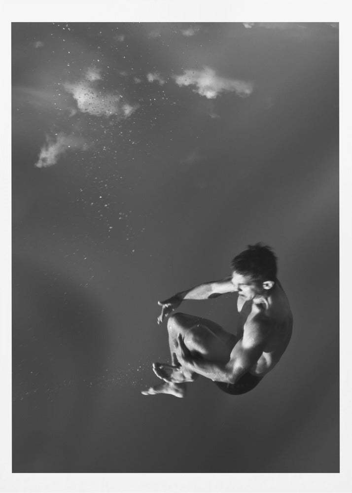 A dramatic black and white photograph of a male diver suspended mid-air in a tuck position. The background is a dark, atmospheric gray, with what appears to be clouds and bubbles, giving the impression of being underwater or in a vast, empty space. The lighting highlights the athlete's muscular physique. Artwork