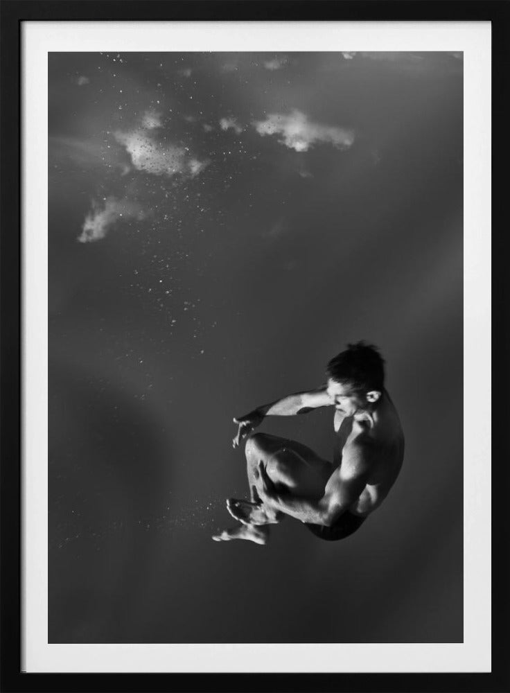 A dramatic black and white photograph of a male diver suspended mid-air in a tuck position. The background is a dark, atmospheric gray, with what appears to be clouds and bubbles, giving the impression of being underwater or in a vast, empty space. The lighting highlights the athlete's muscular physique. Artwork