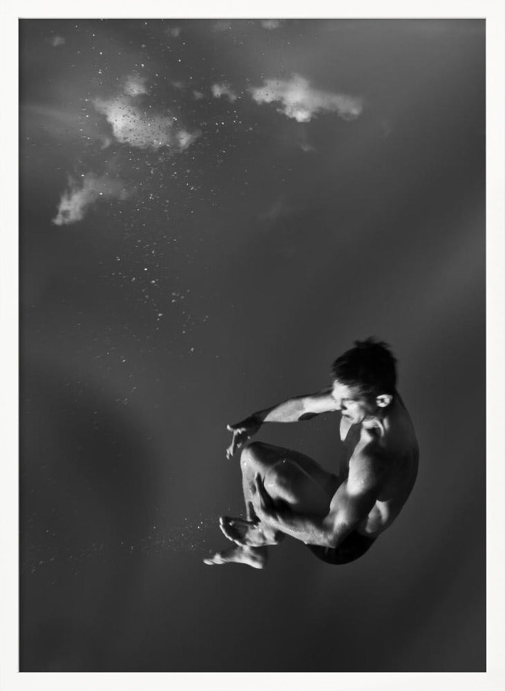 A dramatic black and white photograph of a male diver suspended mid-air in a tuck position. The background is a dark, atmospheric gray, with what appears to be clouds and bubbles, giving the impression of being underwater or in a vast, empty space. The lighting highlights the athlete's muscular physique. Artwork
