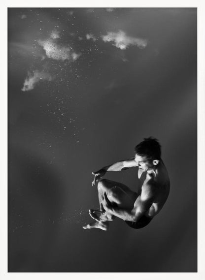 A dramatic black and white photograph of a male diver suspended mid-air in a tuck position. The background is a dark, atmospheric gray, with what appears to be clouds and bubbles, giving the impression of being underwater or in a vast, empty space. The lighting highlights the athlete's muscular physique. Artwork