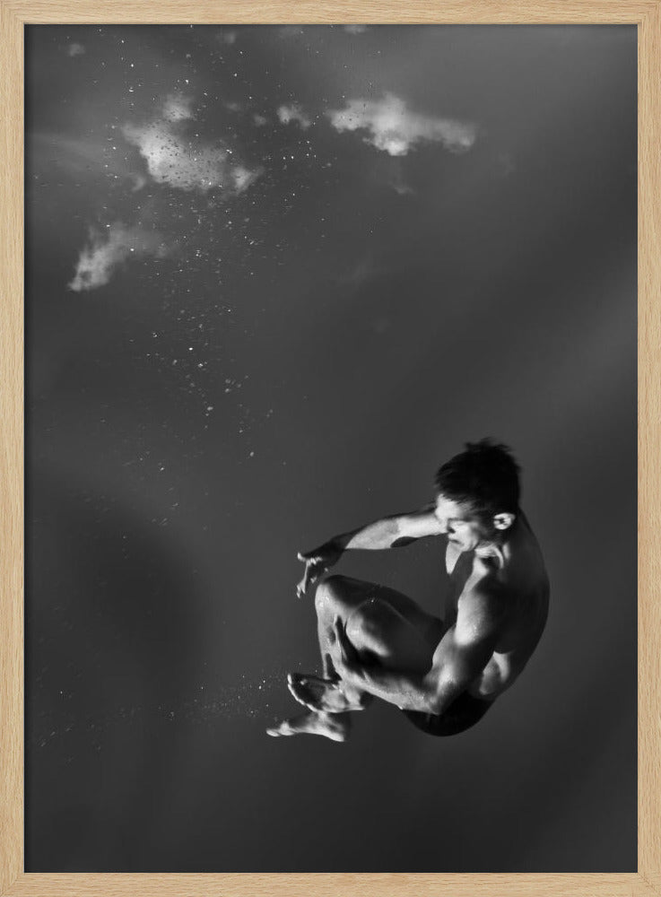 A dramatic black and white photograph of a male diver suspended mid-air in a tuck position. The background is a dark, atmospheric gray, with what appears to be clouds and bubbles, giving the impression of being underwater or in a vast, empty space. The lighting highlights the athlete's muscular physique. Artwork