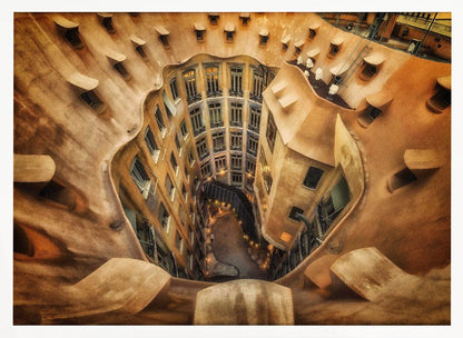 A high-angle, downward view of the inner courtyard of an architecturally unique building, likely Casa Milà by Gaudí. The warm, sandy-colored walls curve and undulate organically, surrounding the multi-story structure with its many windows. The courtyard below is lit, casting a warm glow. Decor