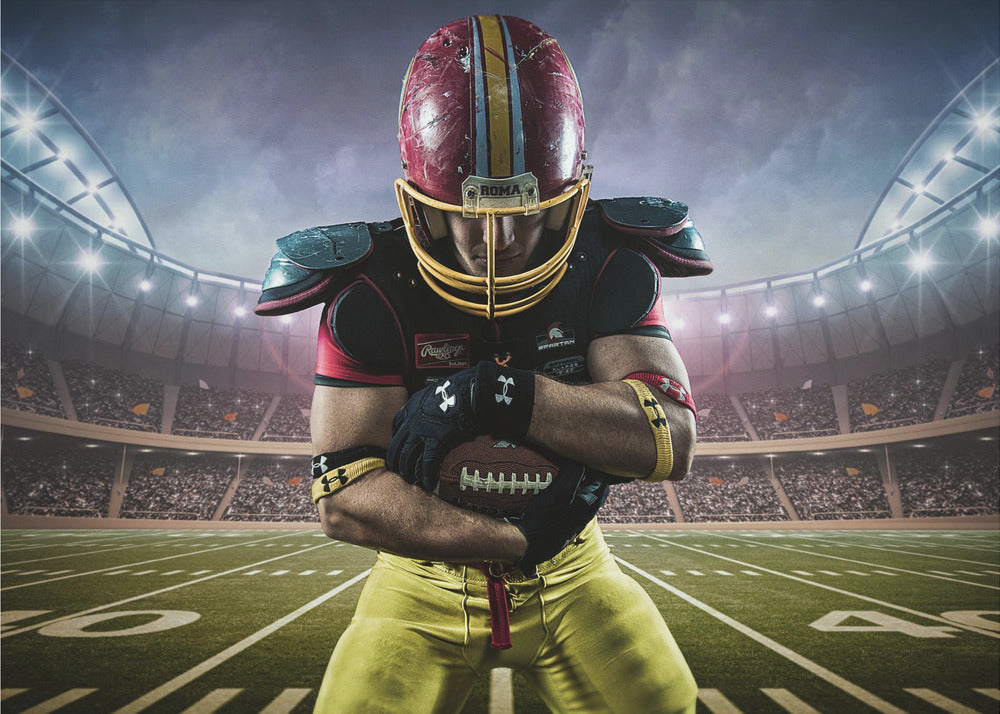 A framed poster of a determined football player in a red and yellow uniform standing on a field in a packed stadium. He is holding a football close to his chest with his head bowed, under bright stadium lights. Decor