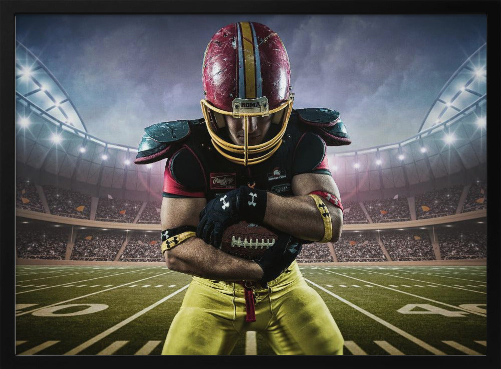 A framed poster of a determined football player in a red and yellow uniform standing on a field in a packed stadium. He is holding a football close to his chest with his head bowed, under bright stadium lights. Decor
