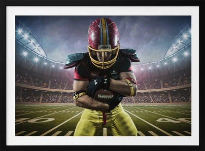 A framed poster of a determined football player in a red and yellow uniform standing on a field in a packed stadium. He is holding a football close to his chest with his head bowed, under bright stadium lights. Decor