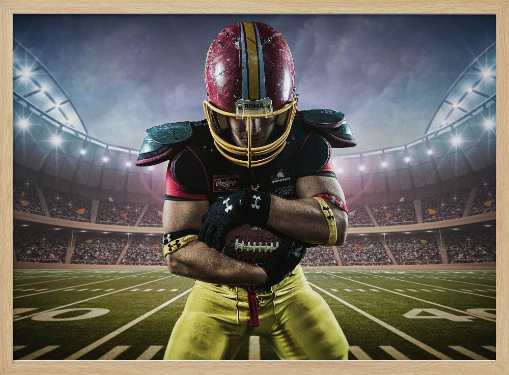 A framed poster of a determined football player in a red and yellow uniform standing on a field in a packed stadium. He is holding a football close to his chest with his head bowed, under bright stadium lights. Decor