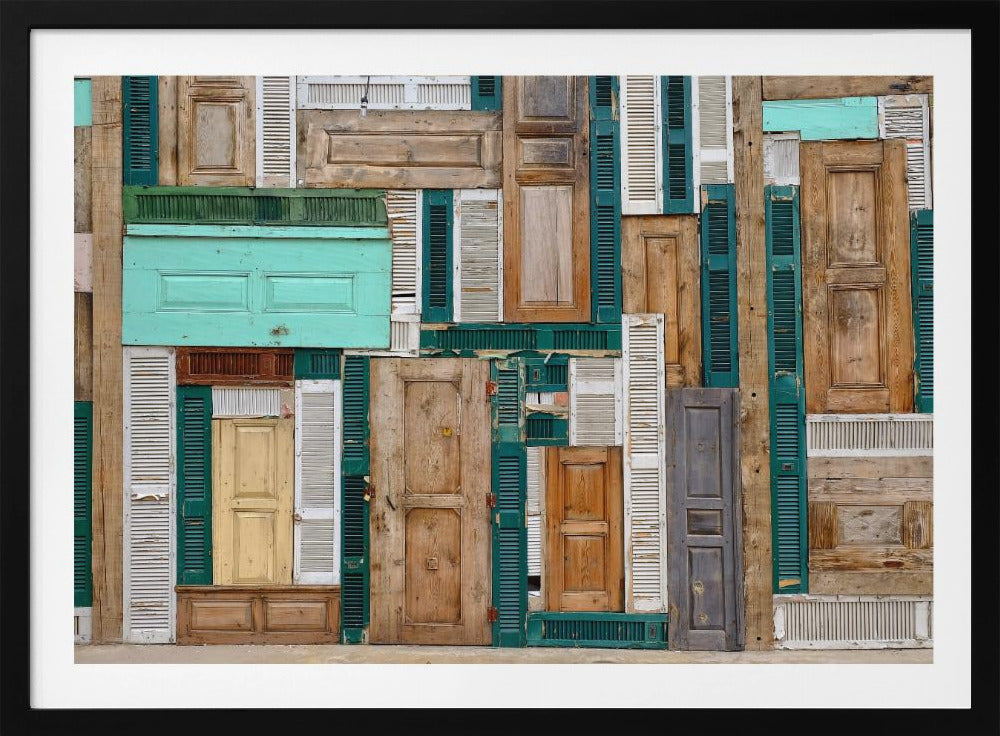 A framed art piece featuring a chaotic collage of various old, weathered wooden doors and window shutters arranged in a dense patchwork, showcasing a rustic texture and colors like natural wood, teal, green, and distressed white. Wall Art