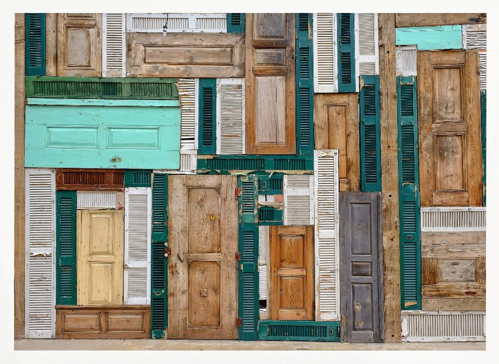 A framed art piece featuring a chaotic collage of various old, weathered wooden doors and window shutters arranged in a dense patchwork, showcasing a rustic texture and colors like natural wood, teal, green, and distressed white. Wall Art