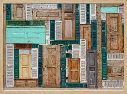 A framed art piece featuring a chaotic collage of various old, weathered wooden doors and window shutters arranged in a dense patchwork, showcasing a rustic texture and colors like natural wood, teal, green, and distressed white. Wall Art