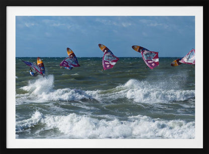 A composite, silver-framed photograph capturing the four stages of a windsurfer's impressive jump over choppy, white-capped ocean waves under a partly cloudy blue sky. Print