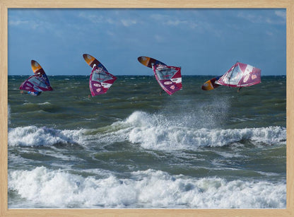 A composite, silver-framed photograph capturing the four stages of a windsurfer's impressive jump over choppy, white-capped ocean waves under a partly cloudy blue sky. Print