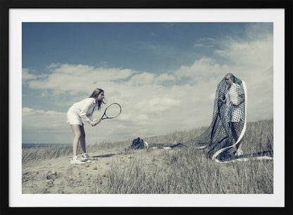 A surreal photograph of two women on a grassy sand dune. One woman is dressed in white tennis attire, bent over and ready to hit a ball with her racket. The other woman stands opposite her, entangled and draped in a large tennis net. The scene is under a cloudy blue sky and has a desaturated, cool-toned color palette, framed in silver. Decor