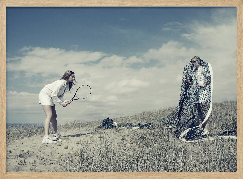 A surreal photograph of two women on a grassy sand dune. One woman is dressed in white tennis attire, bent over and ready to hit a ball with her racket. The other woman stands opposite her, entangled and draped in a large tennis net. The scene is under a cloudy blue sky and has a desaturated, cool-toned color palette, framed in silver. Decor