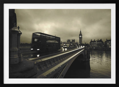 A framed, sepia-toned long-exposure photograph of London. A double-decker bus is shown in motion blur as it crosses Westminster Bridge. In the background, the Big Ben clock tower and the Houses of Parliament are visible against a cloudy sky, with lights reflecting on the wet road and the River Thames. Wall Art