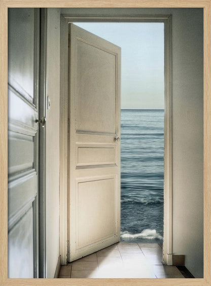 A surreal photograph showing a white interior door swung open, revealing not a landscape but the vast blue ocean, with waves gently washing over the tiled floor of the room. Decor