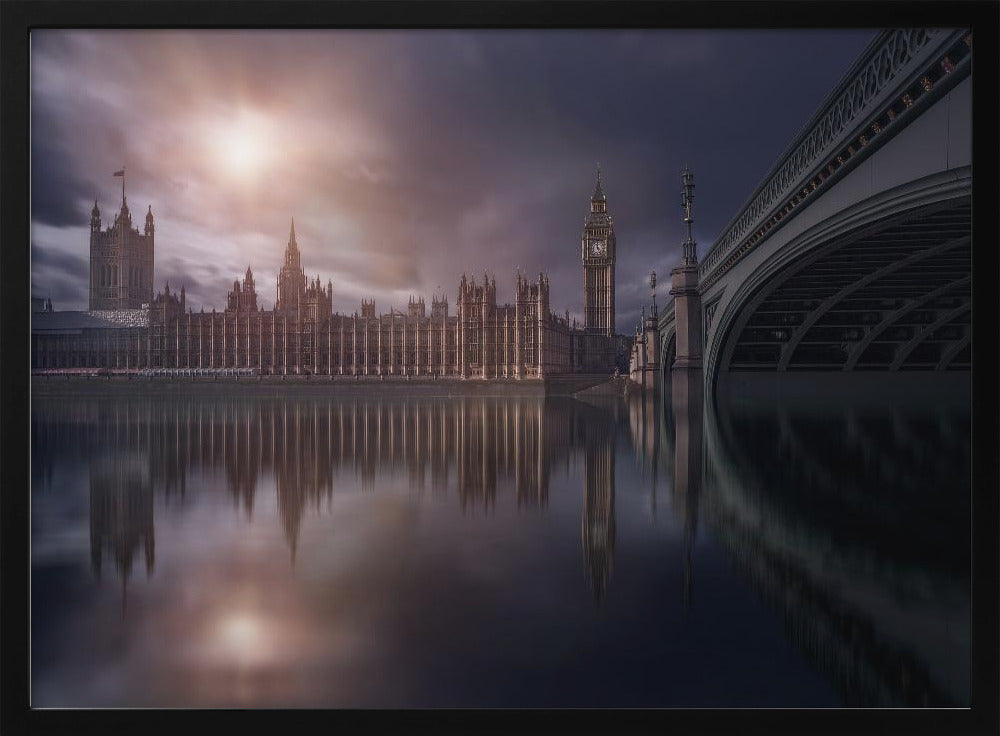 A dramatic, atmospheric photograph of the Houses of Parliament and Big Ben in London, reflected in the still waters of the River Thames. A bright sun breaks through dark, moody clouds, casting a warm light on the scene, with a stone bridge visible to the right. The image is enclosed in a silver frame. Print