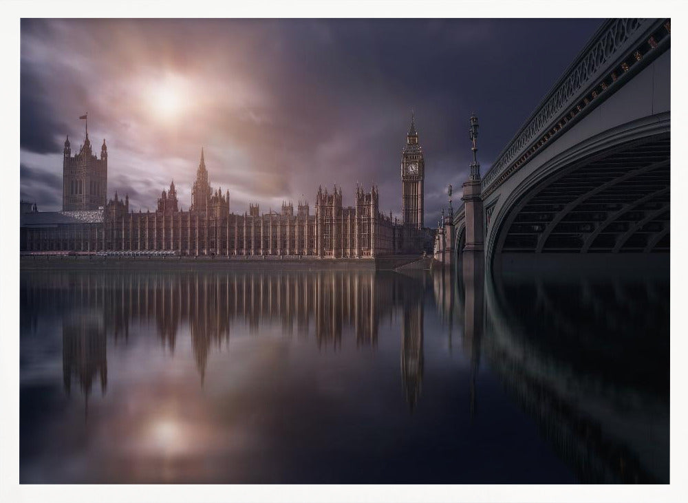 A dramatic, atmospheric photograph of the Houses of Parliament and Big Ben in London, reflected in the still waters of the River Thames. A bright sun breaks through dark, moody clouds, casting a warm light on the scene, with a stone bridge visible to the right. The image is enclosed in a silver frame. Print