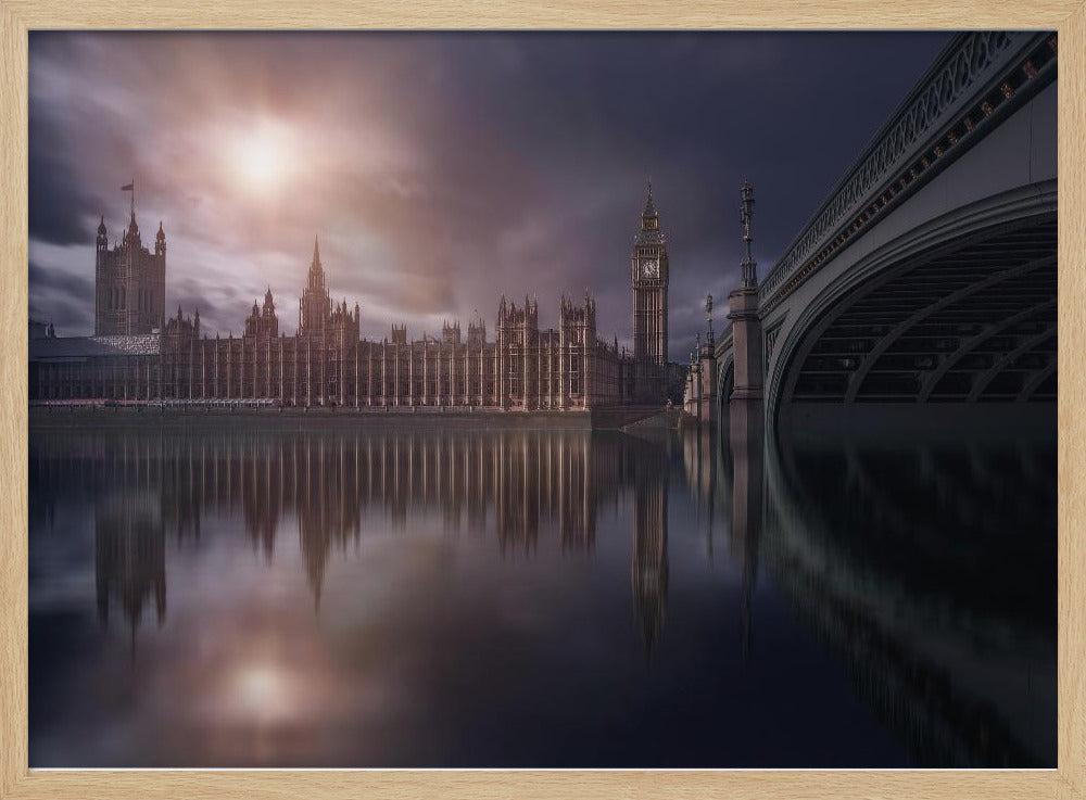 A dramatic, atmospheric photograph of the Houses of Parliament and Big Ben in London, reflected in the still waters of the River Thames. A bright sun breaks through dark, moody clouds, casting a warm light on the scene, with a stone bridge visible to the right. The image is enclosed in a silver frame. Print