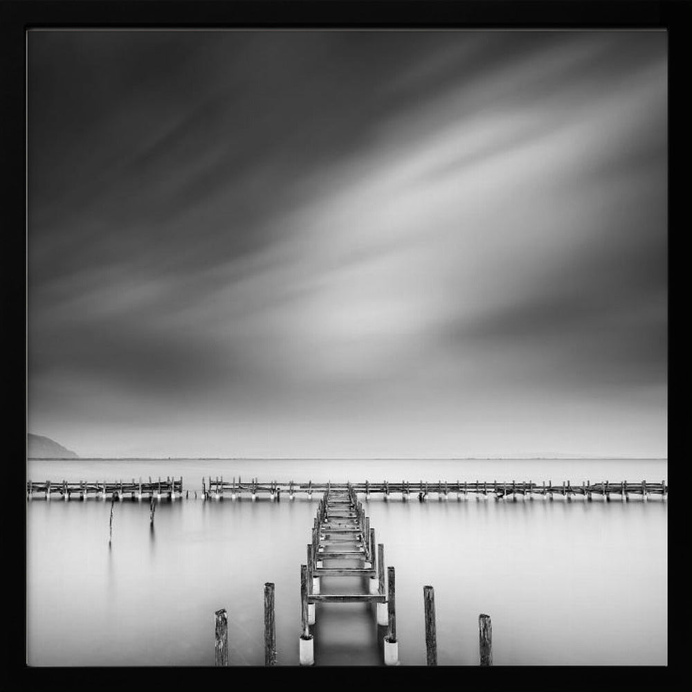 A framed, square black and white long-exposure photograph of a dilapidated wooden pier extending into calm, misty water. The sky is filled with soft, streaked clouds, creating a serene and melancholic mood. Wall Art