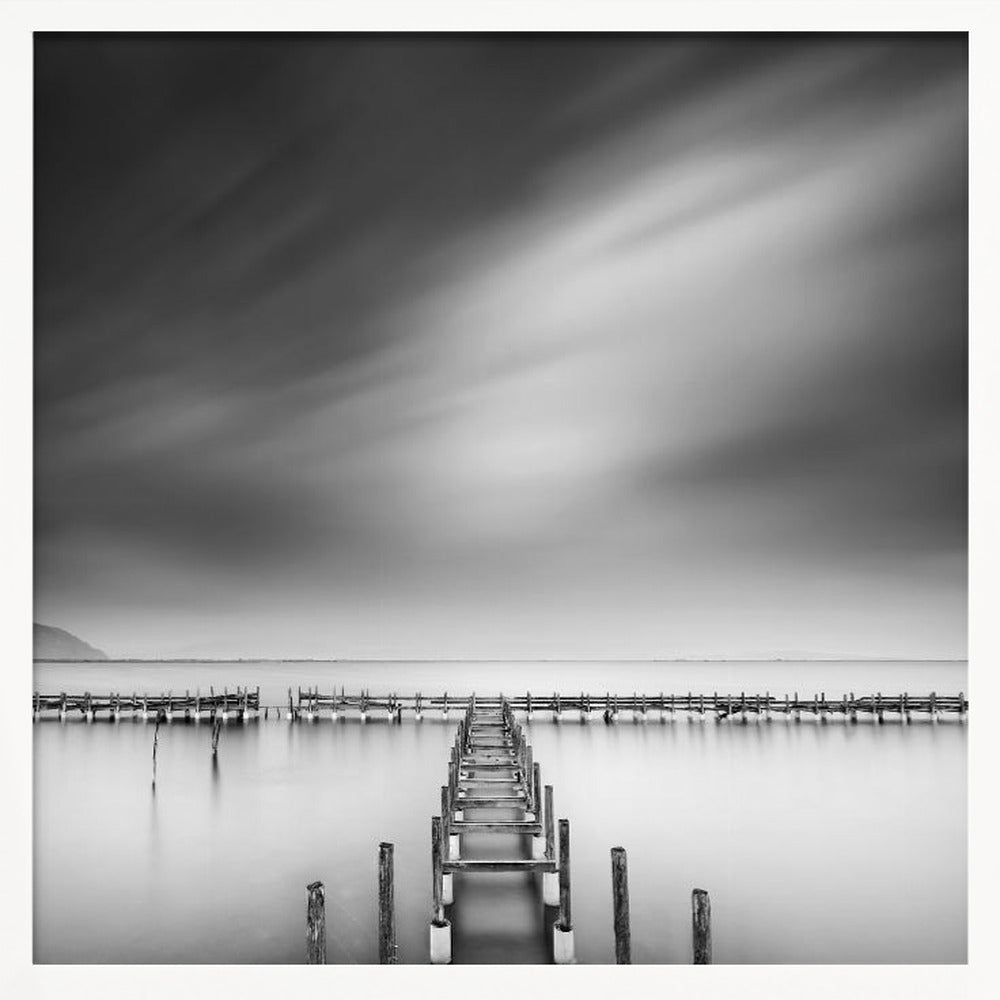 A framed, square black and white long-exposure photograph of a dilapidated wooden pier extending into calm, misty water. The sky is filled with soft, streaked clouds, creating a serene and melancholic mood. Wall Art