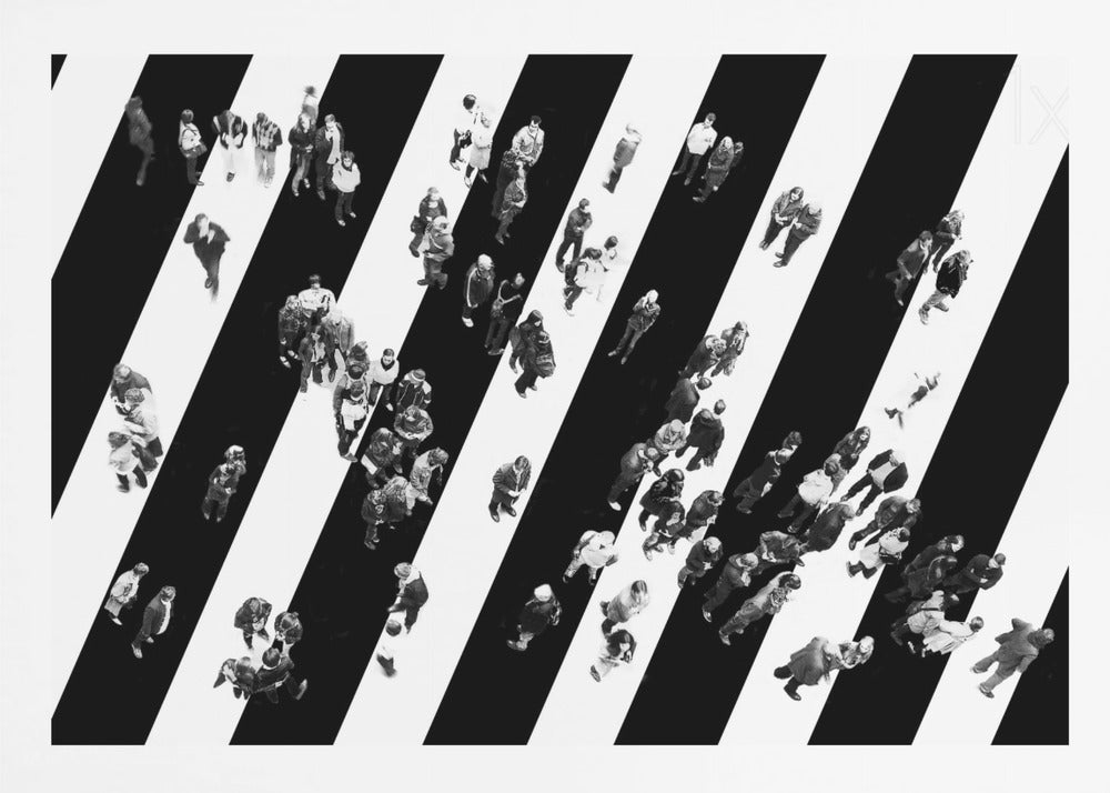 A striking black and white aerial photograph of dozens of people walking across a large, diagonally striped crosswalk. The high-contrast, graphic pattern of black and white stripes dominates the scene, with the small figures of pedestrians scattered across it, creating a sense of movement and urban anonymity. The image is presented within a simple silver frame. Print