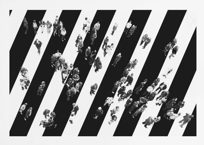 A striking black and white aerial photograph of dozens of people walking across a large, diagonally striped crosswalk. The high-contrast, graphic pattern of black and white stripes dominates the scene, with the small figures of pedestrians scattered across it, creating a sense of movement and urban anonymity. The image is presented within a simple silver frame. Print