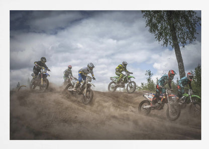 A dynamic action shot of several motocross riders racing up a dirt hill, kicking up a large cloud of dust. The riders are in full gear on colorful bikes, with a dramatic cloudy sky and a tall tree in the background. Print