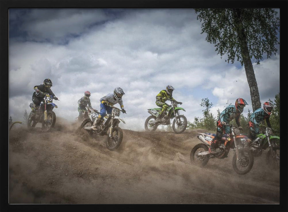 A dynamic action shot of several motocross riders racing up a dirt hill, kicking up a large cloud of dust. The riders are in full gear on colorful bikes, with a dramatic cloudy sky and a tall tree in the background. Print