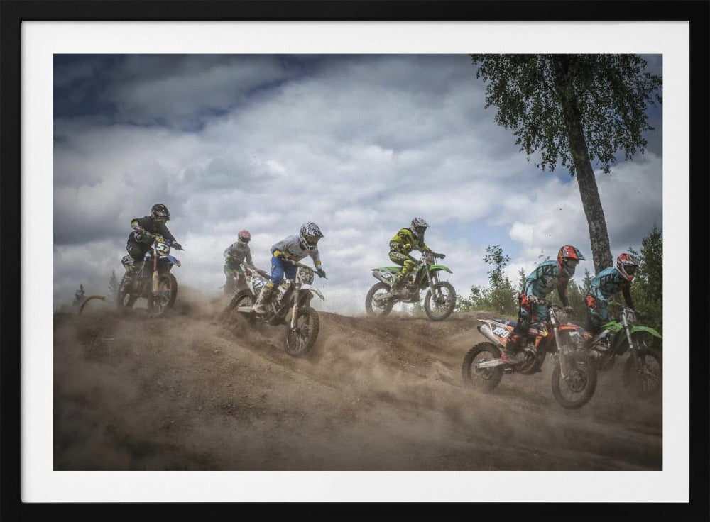 A dynamic action shot of several motocross riders racing up a dirt hill, kicking up a large cloud of dust. The riders are in full gear on colorful bikes, with a dramatic cloudy sky and a tall tree in the background. Print