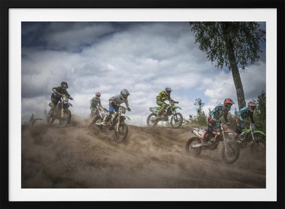 A dynamic action shot of several motocross riders racing up a dirt hill, kicking up a large cloud of dust. The riders are in full gear on colorful bikes, with a dramatic cloudy sky and a tall tree in the background. Print