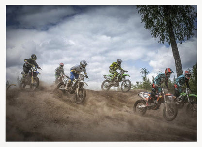 A dynamic action shot of several motocross riders racing up a dirt hill, kicking up a large cloud of dust. The riders are in full gear on colorful bikes, with a dramatic cloudy sky and a tall tree in the background. Print