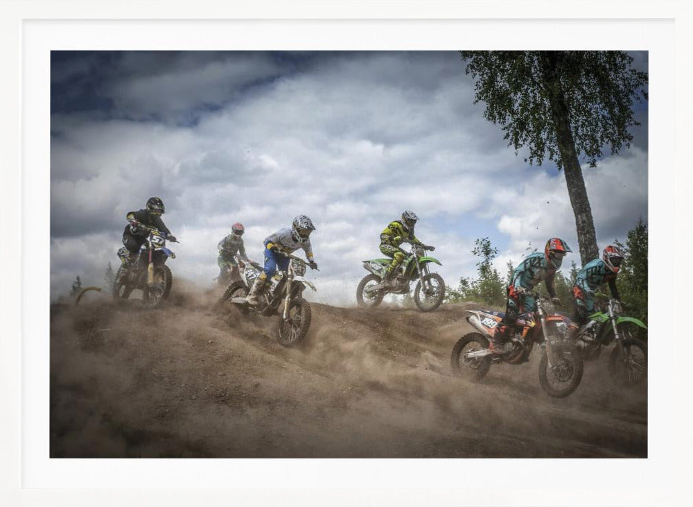 A dynamic action shot of several motocross riders racing up a dirt hill, kicking up a large cloud of dust. The riders are in full gear on colorful bikes, with a dramatic cloudy sky and a tall tree in the background. Print