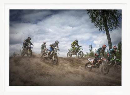 A dynamic action shot of several motocross riders racing up a dirt hill, kicking up a large cloud of dust. The riders are in full gear on colorful bikes, with a dramatic cloudy sky and a tall tree in the background. Print