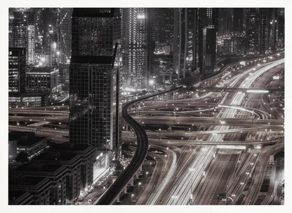 A dynamic black and white long-exposure photograph of a sprawling metropolis at night, viewed from above. Gleaming skyscrapers fill the background, while a complex interchange of highways with streaks of light from traffic dominates the foreground, with an elevated train line weaving through the city. Wall Art