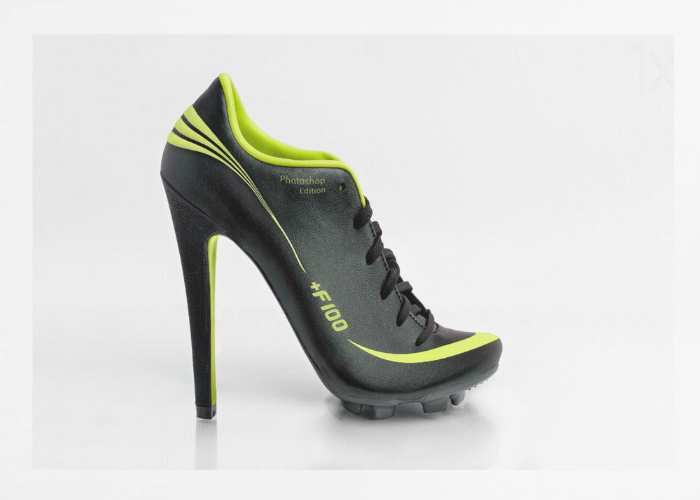 A conceptual piece of digital art featuring a hybrid shoe that is part black soccer cleat and part stiletto high heel. The shoe has neon lime green accents and is displayed against a stark white background inside a silver frame. Decor