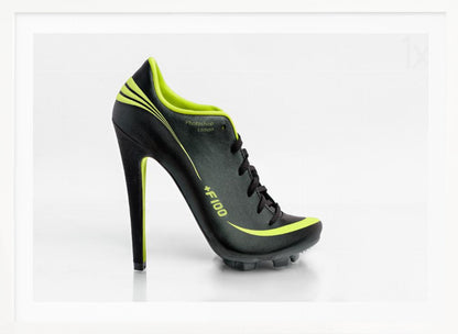 A conceptual piece of digital art featuring a hybrid shoe that is part black soccer cleat and part stiletto high heel. The shoe has neon lime green accents and is displayed against a stark white background inside a silver frame. Decor
