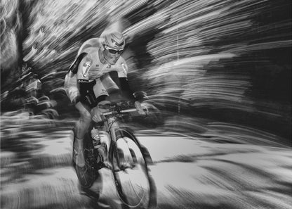 A dramatic black and white action shot of a professional cyclist racing. The cyclist is in focus, wearing a helmet and sunglasses, while the background is a streaky motion blur, creating a powerful sense of speed and movement. The image is enclosed in a silver frame. Wall Art