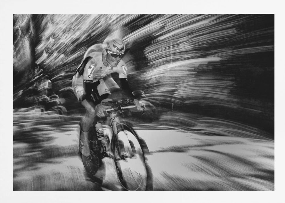 A dramatic black and white action shot of a professional cyclist racing. The cyclist is in focus, wearing a helmet and sunglasses, while the background is a streaky motion blur, creating a powerful sense of speed and movement. The image is enclosed in a silver frame. Wall Art