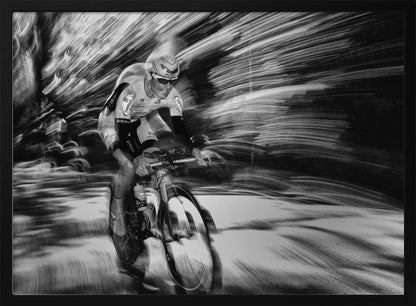 A dramatic black and white action shot of a professional cyclist racing. The cyclist is in focus, wearing a helmet and sunglasses, while the background is a streaky motion blur, creating a powerful sense of speed and movement. The image is enclosed in a silver frame. Wall Art