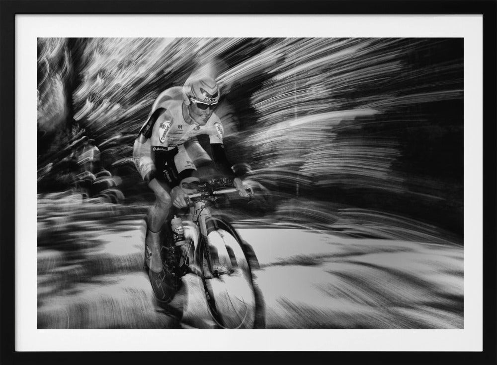 A dramatic black and white action shot of a professional cyclist racing. The cyclist is in focus, wearing a helmet and sunglasses, while the background is a streaky motion blur, creating a powerful sense of speed and movement. The image is enclosed in a silver frame. Wall Art